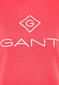 Felpa rosa corallo con collo a costine, caratterizzata da un logo a diamante bianco con una 'G' e la parola "GANT" ricamata in bianco.