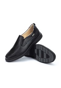 Zapatos de cuero negro sin cordones con un acabado suave, puntera redondeada y suela de goma texturizada con acentos de agarre. Detalle de costura lateral sutil.