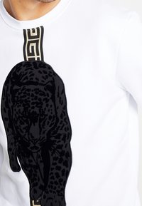 Sudadera blanca con un gran diseño de un pantera negra caminando hacia abajo a lo largo de una franja geométrica vertical en el pecho.