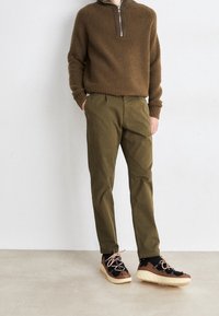 Brun ribbad stickad tröja med halvdragkedja, olivgröna byxor och svarta/bruna sneakers med beige sula och rosa snören.