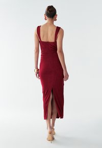 Crvena midi haljina s podesivim trakama, prilagodljivim dekolteom i zatvaračem na leđima. Sadrži visoki prorez, mekan teksturiran materijal i elegantan kroj.