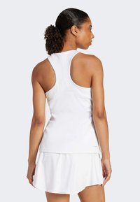 Hvid atletisk tanktop med racerback-design og en lagdelt hvid nederdel. Glat stof med en let glans. Ingen synlige logoer eller mønstre.