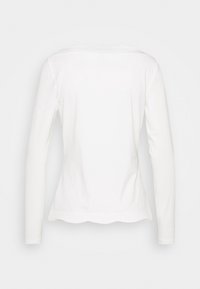 White long-sleeve women's shirt shown from the back, with a scalloped hem and a smooth, fitted design.