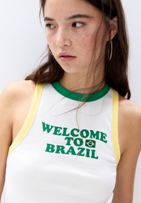 Ribbede hvid tanktop med grønne og gule kanter, med teksten "VELKOMMEN TIL BRASILIEN" og et lille brasiliansk flaggrafik.