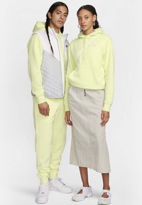 Due individui indossano abbigliamento sportivo di un giallo brillante. L'uomo ha un gilet grigio gonfiato, mentre la donna abbina una felpa gialla a una gonna leggera.