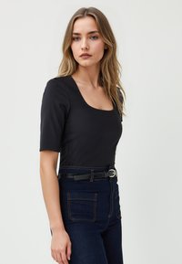 Zwart aangesloten top met een vierkante halslijn, korte mouwen en een egale textuur, gecombineerd met hooggerokte donkere denim jeans met twee achterzakken.