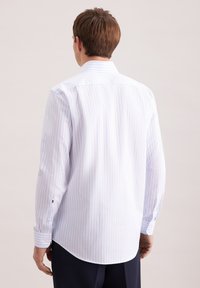 Biała koszula zapinana na guziki z jasnoniebieskimi pionowymi paskami, długimi rękawami i zaokrąglonym dołem. Posiada klasyczny kołnierzyk i mankiety na guziki.