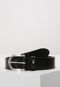 Ceinture en cuir noir avec une boucle en métal argenté, présentant un accent de logo et une texture lisse. Le design est simple et classique.