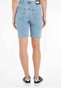 Shorts de mezclilla en azul claro, con un dobladillo desgastado y bolsillos traseros. La cintura cuenta con una etiqueta de marca con acentos en rojo, blanco y azul.