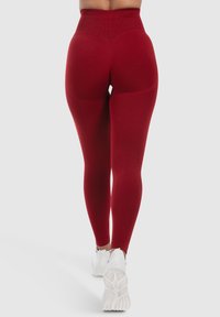 Hooggesneden rode leggings van rekbaar materiaal, met een gladde textuur en contourseam details, gecombineerd met witte sportschoenen.