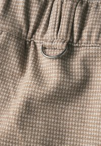 Tessuto marrone con motivo a diamante; presenta una vita arricciata e un accento in metallo argentato a forma di anello. Texture morbida e aspetto leggero.