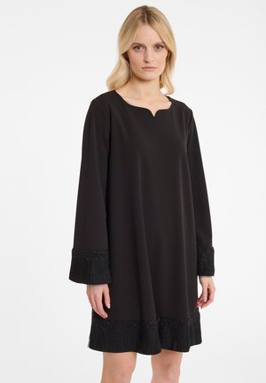 Schwarzes Kleid mit einem dezenten V-Ausschnitt, langen Ärmeln und strukturierten Fransenärmeln, die mit Perlen verziert sind. Glattes Material mit lockerer Passform.