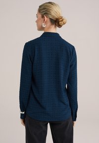 Camisa de manga larga azul marino con patrón texturizado, cuello y puños abotonados. La tela parece suave con un ligero brillo, diseñada para un ajuste relajado.