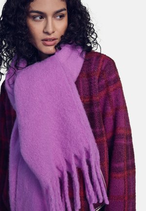 Lila ullsjal med fransade ändar som ligger över en vinröd och rutmönstrad jacka, vilket visar på en mjuk textur och rika färger.