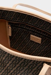 Große beigefarbene Handtasche mit gemustertem schwarzem Innenfutter, Reißverschlusstasche, Lederakzenten und Logotag. Glatte Textur mit verstärkten Nähten.