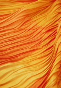 Textilný materiál v odtieňoch oranžovej a žltej, s vertikálnymi záhybmi, ktoré vytvárajú štruktúrovaný, plynulý vzhľad. Mäkko, ľahký materiál.