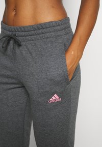 Grijze joggerbroek van zacht materiaal, met een trekkoord in de taille en zijzakken, met een roze Adidas-logo op het linkerbeen.