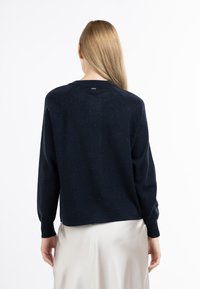 Marineblå sweater fremstillet af tekstureret materiale, med lange ærmer, rund halsudskæring og en let cropped pasform. Bagsiden viser et minimalt brandingdetalje.