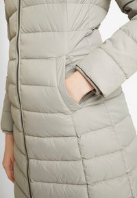 Gevoerde, lichtgrijze jas met een rits aan de voorkant, zijzakken en geribde manchetten met horizontale stiksels voor isolatie.