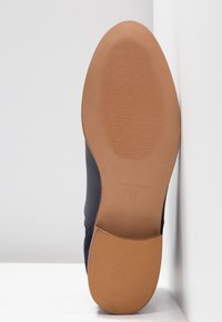 Semelle d'une chaussure en cuir noir montrant une semelle extérieure lisse de couleur beige avec une texture antidérapante, taille 37, et "Fabriqué en Espagne" embossé.