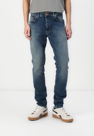 Bleka blå denimjeans med slim fit, femficksdesign och kopparfärgad hårdvara. Bärs med ljusa sneakers med svarta detaljer.