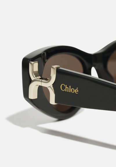 Schwarze Sonnenbrille mit braunen Gläsern, mit einem goldenen Akzent am Bügel und dem Markennamen "Chloé" in Gold auf dem Scharnier eingraviert.