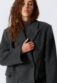 Grå ullblandingsfrakk med dobbel spent design, brede revers og store knapper. Har en teksturert finish og sidelommer.