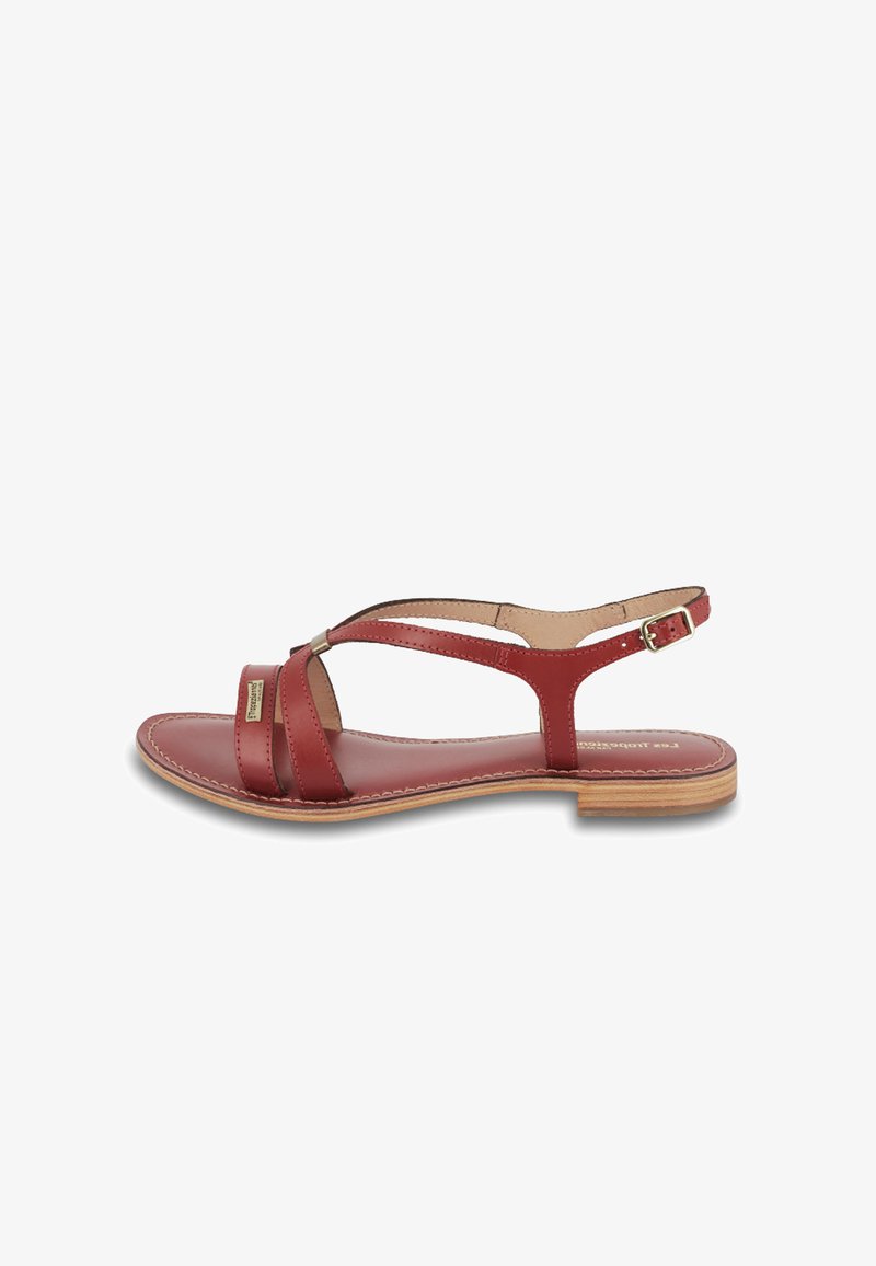 Rode leren sandaal met een vlakke zool, gekruiste bandjes en een enkelband met een gesp. Gladde textuur en minimalistisch ontwerp.