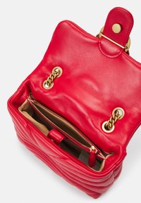 Borsa in pelle rossa con design trapuntato. Presenta un interno color marrone chiaro, hardware dorato e un compartimento con zip. Apertura superiore con chiusura a scatto.