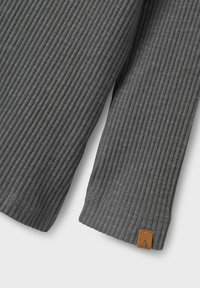 Grå randig långärmad tröja som framhäver den texturerade tyget, rundad nederkant och en liten läderetikett med ett präglat bokstav 'A'.