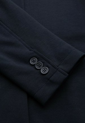 Gros plan sur la manche d'un blazer bleu marine foncé avec trois boutons assortis disposés verticalement près du poignet.