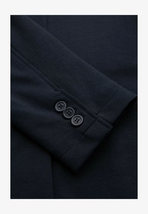 Gros plan sur la manche d'un blazer bleu marine foncé avec trois boutons assortis disposés verticalement près du poignet.