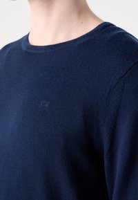 Maglione lavorato a maglia blu navy realizzato in un tessuto morbido, con scollo rotondo e un discreto logo "CK" al centro davanti.