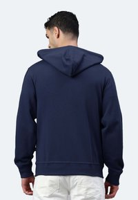 Felpa con cappuccio blu navy con polsini e orlo a costine, dotata di un ampio cappuccio morbido e una trama liscia, mostrata da dietro.