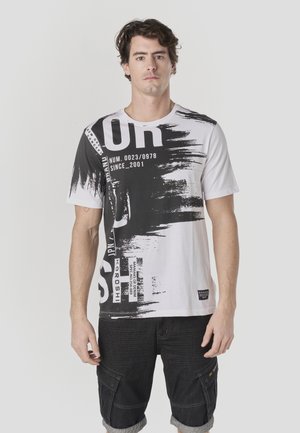 Camiseta de manga corta en blanco y negro con estampados gráficos, elementos de texto y diseños de brochazos de pintura. Combina con pantalones cortos cargo oscuros.