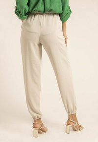Pantalons beige évasés avec une taille élastique et des chevilles ajustées, fabriqués à partir d'un tissu léger. À associer avec des sandales à talons blocs ouvertes dorées.