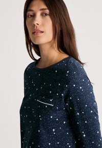 Camicia a maniche lunghe blu navy con motivo a stelle, scollatura rotonda e una piccola tasca sul petto con bordi in contrasto. Tessuto dalla texture liscia.