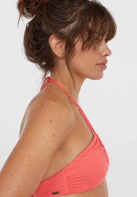 Koraalkleurige bikini top met een geplooid ontwerp, dunne bandjes en een gladde textuur. Kenmerken zijn zichtbare stiksels en een klein logo-label.