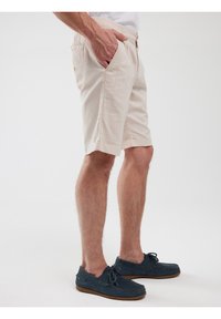 Beige puuvillashortsit, joissa on rento malli, sivutaskut ja litteä vyötärö, yhdistetty tummansinisiin mokka-bootsit.