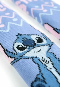 Calzini a maglia blu e rosa con un personaggio dei cartoni animati dai grandi occhi, su uno sfondo a pastello decorato.