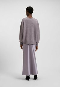 Przesadnie duży, jasnofioletowy sweter dzianinowy z prążkowanym wykończeniem, zestawiony z lekką satynową spódnicą w odcieniu lawendy, posiadającą boczne rozcięcie i długość do kostek.