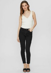 Biała, prążkowana bluzka na ramiączkach z dekoltem w kształcie litery V, zestawiona z czarnymi rurkami i czarnymi klapkami. Gładka struktura i dopasowany krój.