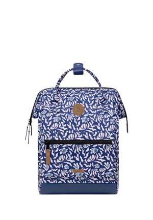 Blue and white floral-patterned backpack with a front zipper pocket, top handle, and brown leather logo patches.