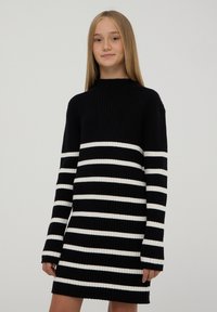 Abito maglione nero a coste con strisce orizzontali bianche, caratterizzato da un colletto alto e maniche lunghe, con una vestibilità comoda alla lunghezza del medio coscia.