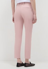 Person wearing slim-fit pink pants and black mesh flats standing against a plain white background.