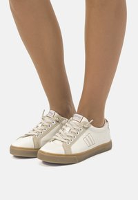Zapatillas de piel blanca con detalles en beige, suela de goma y diseño de cordones. Logotipo de la marca notable cosido en un lado.