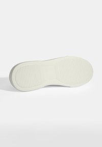 White rubber shoe sole with textured grip patterns and a rounded edge. Smooth finish with defined heel and midsole grooves.