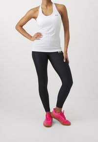 Canotta sportiva bianca con design a racerback, abbinata a leggings neri. Sneakers rosa con dettagli testurizzati e suole in gomma.