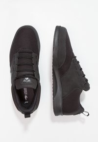 Une paire de baskets Lacoste Sport noires avec des panneaux en mesh et en daim, des lacets et des semelles en caoutchouc, présentée avec des vues de dessus et de côté sur fond blanc.