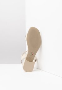 Sandal con tacco beige, realizzata con tomaia in pelle liscia, suola in gomma testurizzata e cinturini minimalisti. Progettata per comfort e stile.